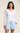 A woman modeling a white long-sleeve V-neck top and light blue drawstring shorts against a plain beige studio background.