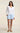A woman modeling a white long-sleeve V-neck top and light blue shorts against a plain beige studio background.