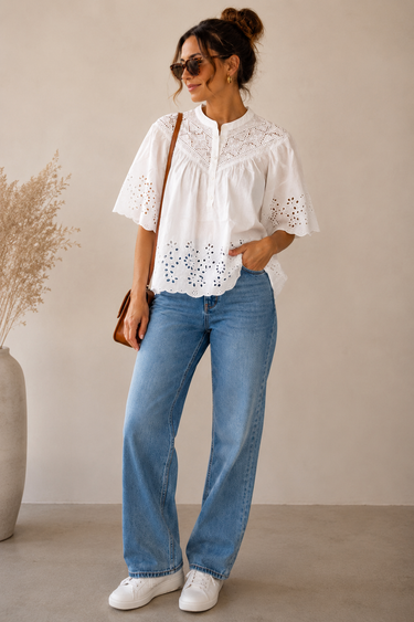 Woman wearing a white blouse with lace details and blue jeans against a beige background