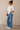Woman wearing a white blouse with lace details and blue jeans against a beige background