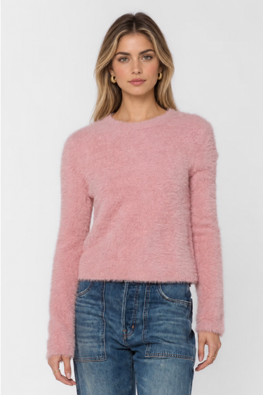 A woman modeling a fuzzy, long-sleeve crewneck sweater in dusty pink, paired with blue jeans, against a plain light gray background.