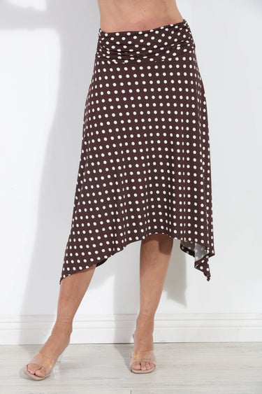 A brown and white polka dot wrap midi skirt worn by a model, shown from the waist down against a white wall.