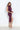 A woman wearing a plum sleeveless ruched midi dress with a draped neckline and thigh-high side slit, styled with neutral heels.