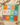 A square patchwork-style cotton bandana laid flat on a beige surface, featuring a grid of colorful tropical and sun motifs in orange, blue, pink, green, and teal. The cloth is styled with draped cream fabric, a small dish, and dried flowers around it.