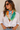 A woman wearing a white button-down shirt and sunglasses, styled with a colorful patchwork-print neck scarf featuring green, blue, orange, and cream panels.