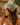 A woman wearing a tropical beach-themed printed headscarf with 'Paradise Beach' text, featuring palm trees, flamingos, and a blue ocean design.