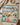 A square fabric map-style print bandanafeaturing illustrated landmarks and routes across the United States, laid flat on a beige surface with a cream blanket, small photo card, and other props around it.