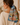 A woman wearing a cream ribbed knit sweater, shown from the back in profile. Her brown hair is tied back in a ponytail with a square cotton scarf featuring a colorful vintage map illustration of Route 66 and Southwest US landmarks.