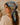 A woman in profile wearing a light blue cotton scarf with a colorful vintage-style map print and Route 66 graphics, paired with a cream ribbed knit sweater in a softly lit indoor setting