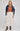 Woman wearing a rust top, white pleated skirt, and blue jacket on a plain background