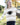 A woman wearing a beige and cream striped knit sweater with a black football graphic on the chest, standing outdoors in a grassy area with trees in the background.