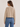Woman wearing a beige sweater and blue jeans on a plain background