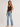A woman modeling a dark brown ribbed knit tank top and light blue straight-leg jeans against a plain light gray studio background.