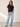 A woman modeling a black short-sleeve knit top and light-wash wide-leg jeans against a neutral studio backdrop.
