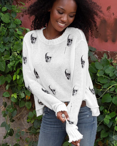 A woman wearing sunglasses and a white distressed skull printed knit sweater.