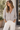 Woman wearing a light oatmeal marled V-neck button-front cardigan with white wide-leg jeans.