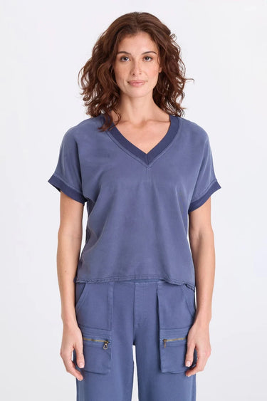 A woman wearing a blue twill v-neck short sleeve top and matching cargo pants on a white background.