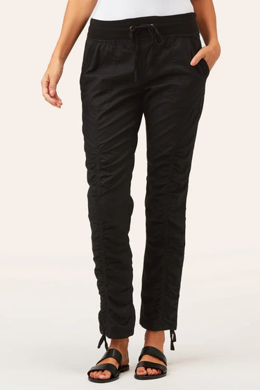 Black drawstring pants with ruched side details and ankle ties, shown on a model wearing black sandals against a light beige studio background.