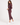 A woman modeling a matching burgundy athletic tracksuit, featuring a zip-up jacket and cropped pants, paired with white sneakers, against a plain white studio background.