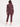 A woman modeling a matching burgundy athletic tracksuit, featuring a zip-up jacket and cropped pants, paired with white sneakers, against a plain white studio background.