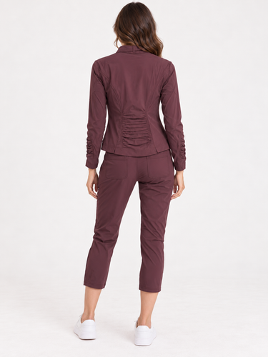A woman modeling a matching burgundy athletic tracksuit, featuring a zip-up jacket and cropped pants, paired with white sneakers, against a plain white studio background.