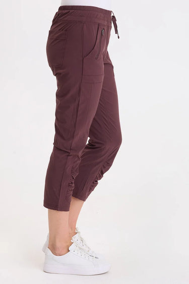 A side angle of a woman wearing leggings with drawstring waist with zippered mini pockets team up with ruched front leg panels, front/back pockets and a cropped silhouette.
