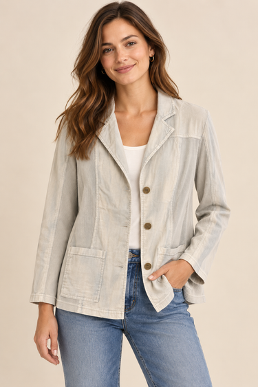 A woman modeling a light beige linen-blend blazer with brown buttons, worn over a white top and blue jeans, against a solid beige background.