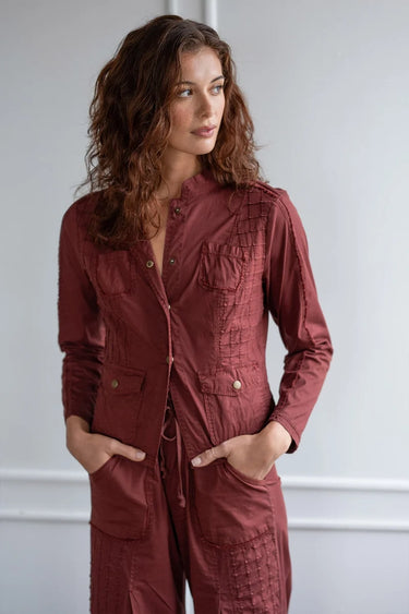 A woman wearing a blazer sports grid pintucking, rib contrast panels and brass hardware and matching berry pants on a white background.