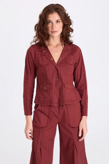 A woman wearing a blazer sports grid pintucking, rib contrast panels and brass hardware and matching berry pants on a white background.