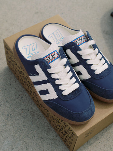 A pair of blue and white retro-style low-top sneakers resting on a brown patterned shoebox, placed on a gray concrete floor.