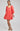 Woman wearing a coral dress with lace details on a plain background