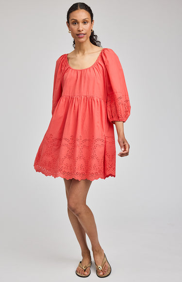 Woman wearing a coral dress with lace details on a plain background