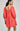 Woman wearing a coral dress with intricate cut-out details on a plain background