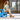 Woman sitting on a blue chair outdoors, wearing a light dress and sandals.