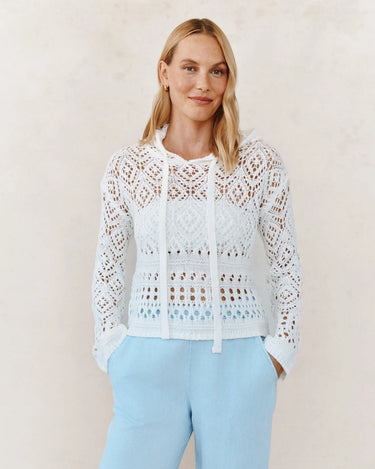 Woman wearing a white lace top and light blue pants against a plain background
