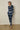 Person wearing a blue tie-dye outfit standing against a plain wall.