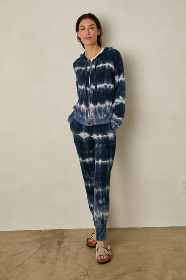 Person wearing a blue tie-dye outfit standing against a plain wall.