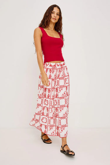 Woman wearing a red top and white patterned skirt on a white background