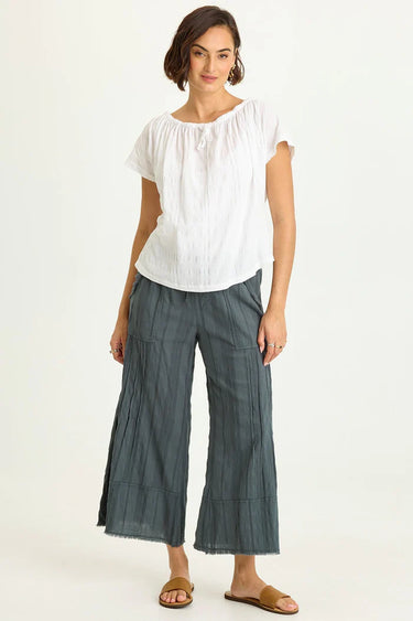 Woman wearing a white blouse and gray wide-leg pants on a white background