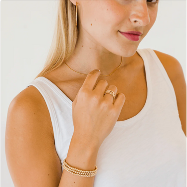 A person is wearing a gold-colored bracelet with small beads on their wrist. The bracelet appears to be made of metal, likely gold-filled, and is part of a waterproof jewelry collection.