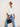 A woman modeling a cream-colored, oversized button-down shirt tied at the waist, paired with blue denim jeans on a white background