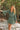 woman wearing floral dress holding onto a tree standing on a sandy beach