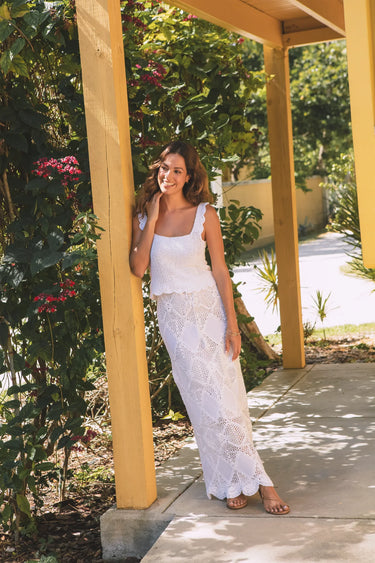 women wearing scallop crochet tank and maxi skirt leaning on a post with flowers in the background