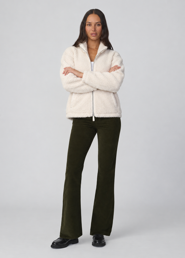 Front view of Joe’s Jeans Inez Corduroy Bootcut Pant in Olive showing mid-rise waist and full-length fit with a cream sherpa zip up jacket.
