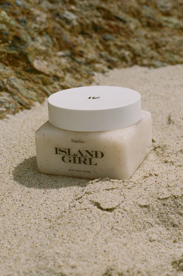 Jar of 'Island Girl' body scrub on sand with natural background