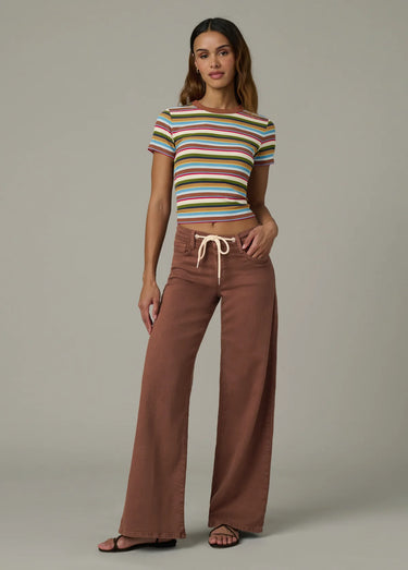 Woman wearing a striped crop top and brown wide-leg pants on a plain background