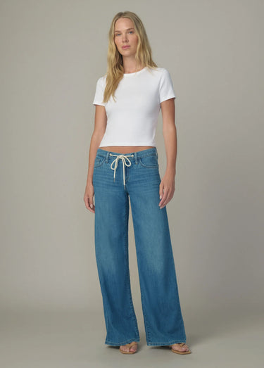 Woman wearing a white top and blue jeans against a neutral background