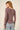 Woman wearing a long-sleeve brown top and jeans on a beige background