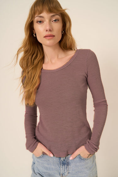 Woman wearing a long-sleeve mauve top against a beige background