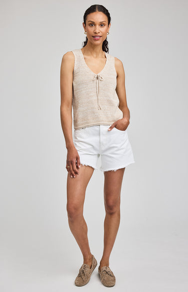 Woman wearing a beige sleeveless top and white shorts on a plain background